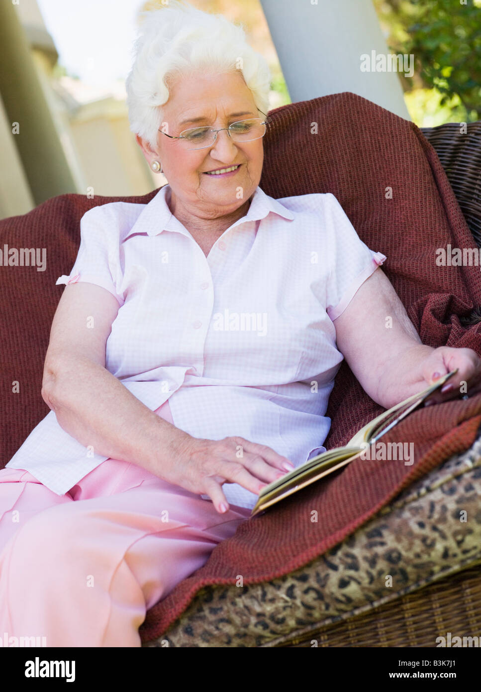 Senior woman sitting outdoors on a chair reading a book Stock Photo - Alamy