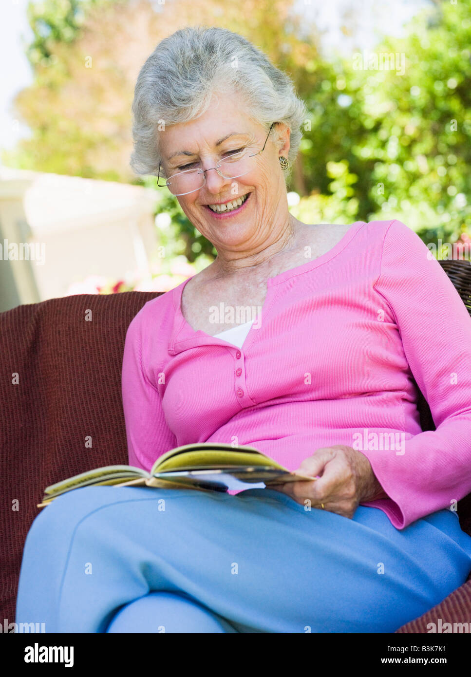 Senior woman sitting outdoors on a chair reading a book Stock Photo - Alamy