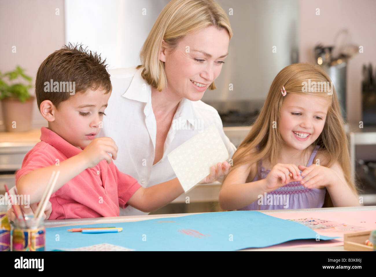 Woman and two young children in kitchen with art project smiling Stock Photo