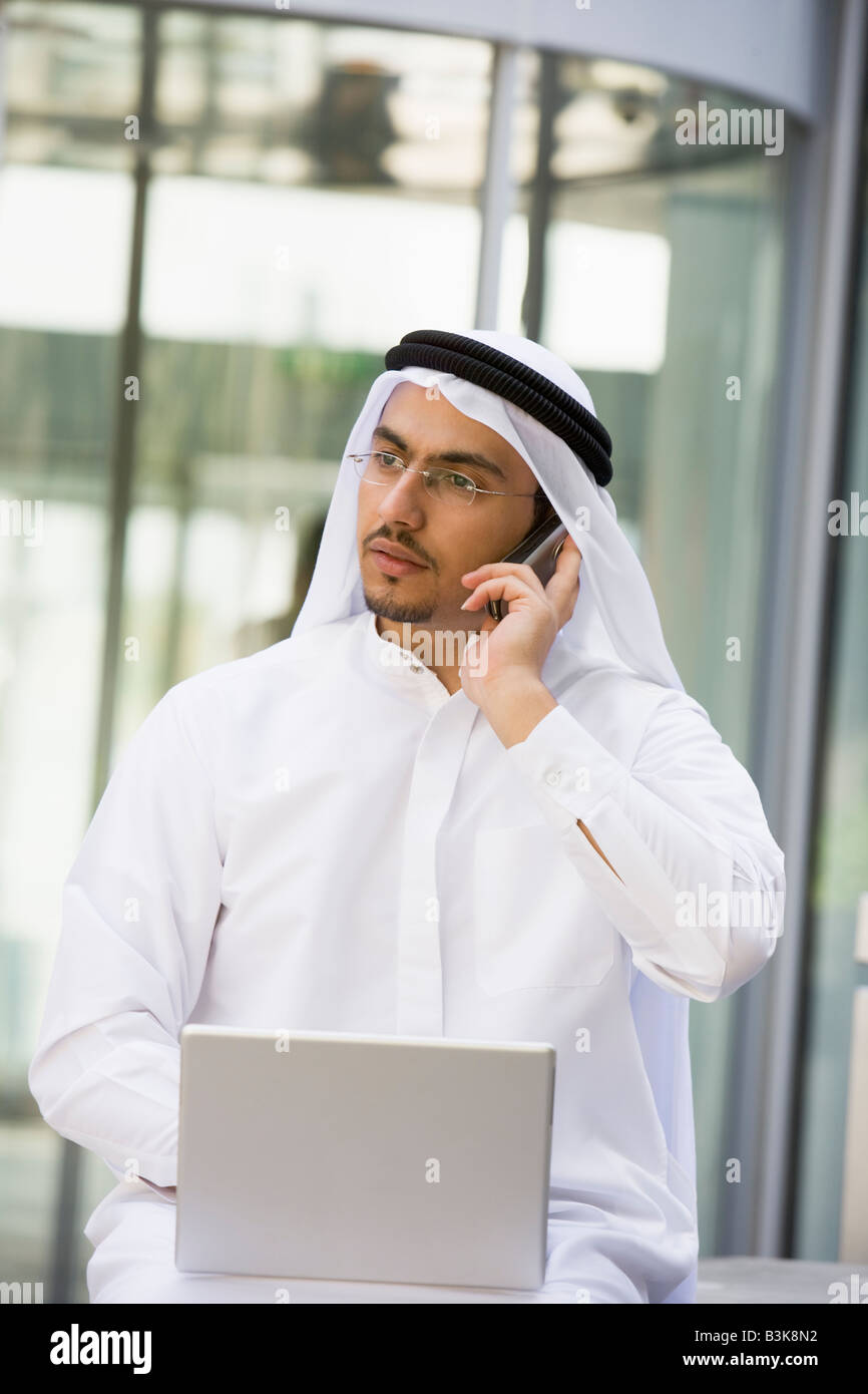 Man outdoors with laptop and cellular phone by building (selective focus) Stock Photo