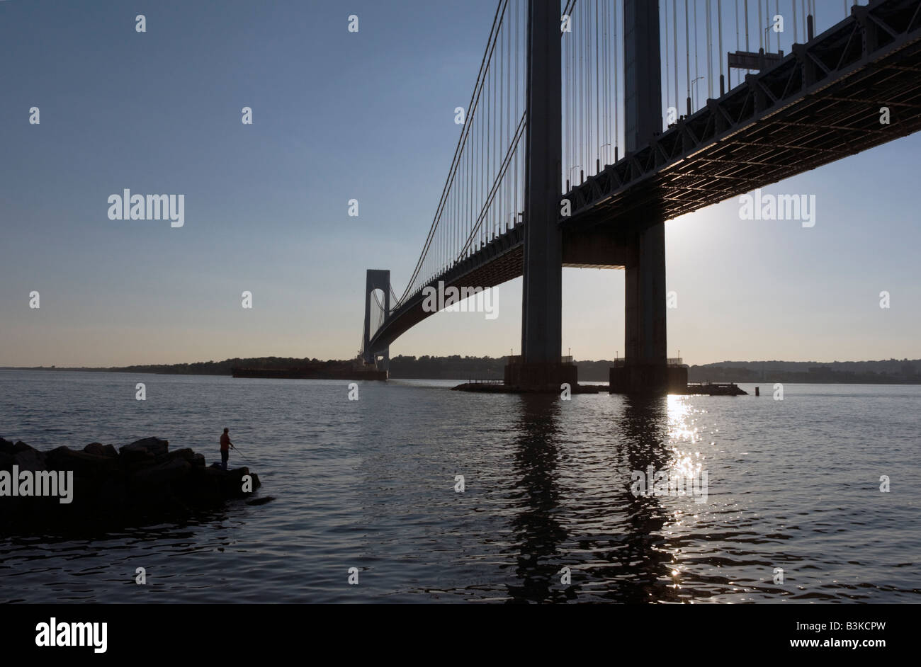A man fishes off a reef at the Brooklyn side of the Verrazano Bridge Staten Island on the horizon Stock Photo