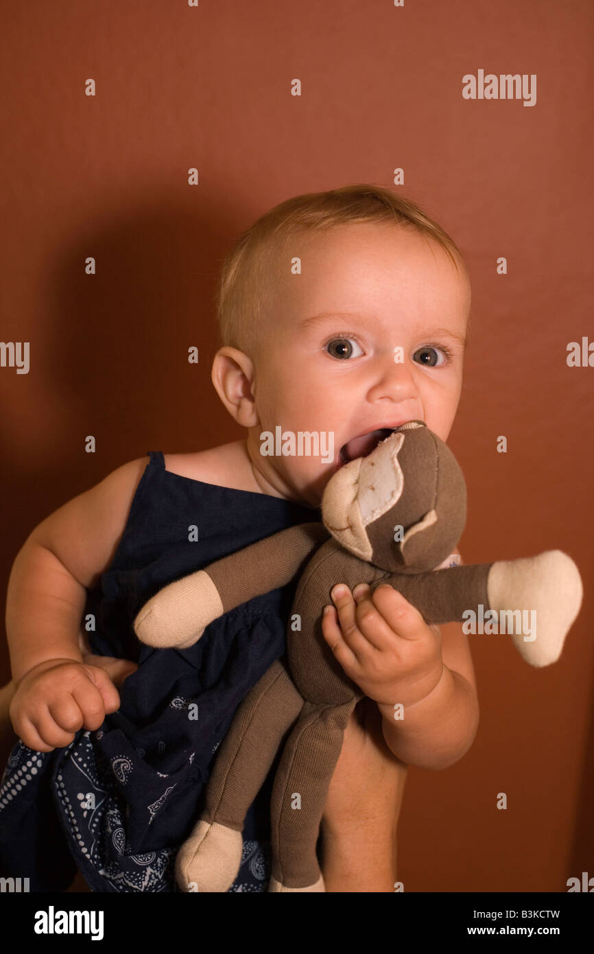 eight month old baby girl biting her favorite stuffed animal monkey toy, daughter, younger sibling, sister Stock Photo