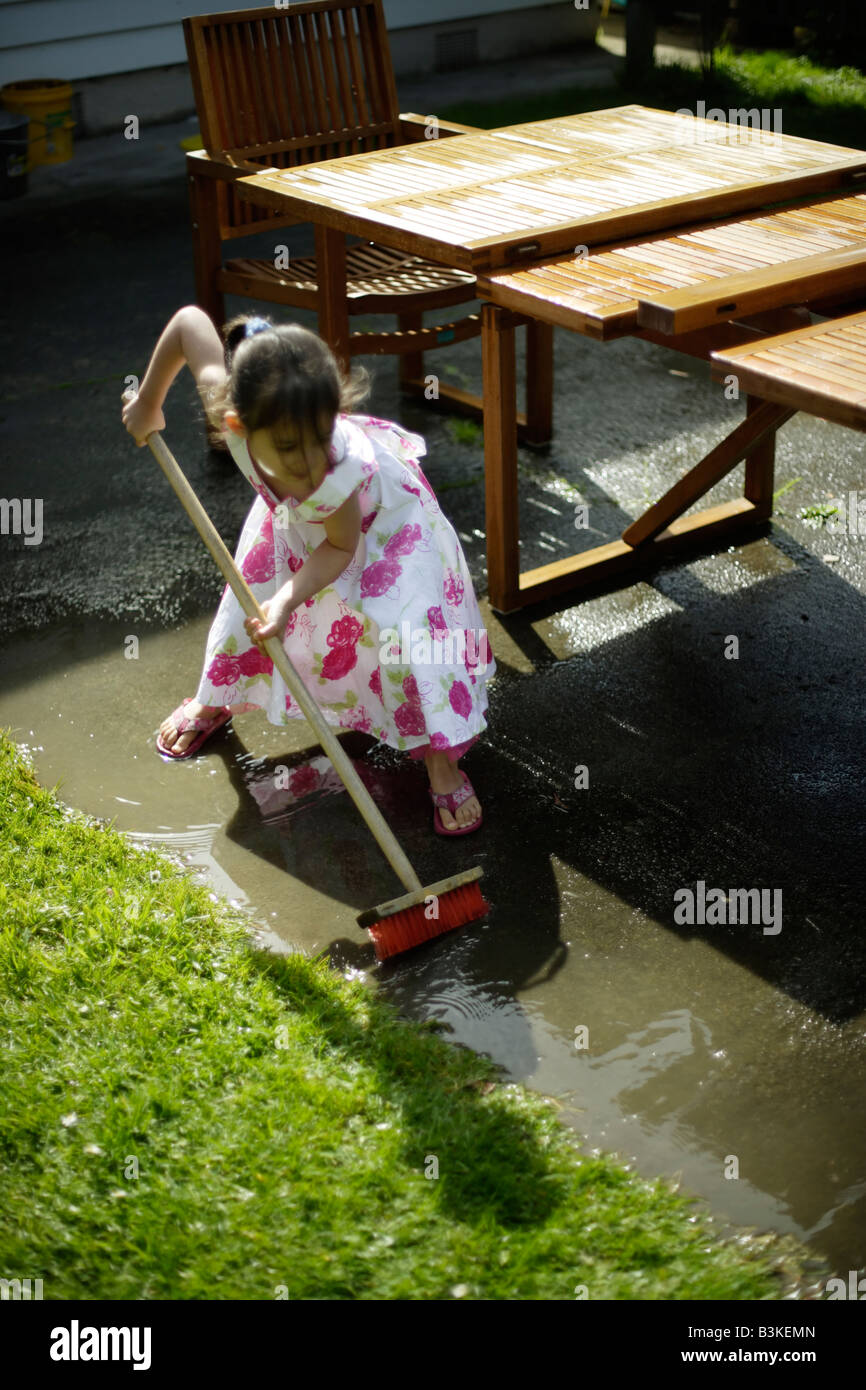 Sweeping away the water Girl aged five with broom Stock Photo