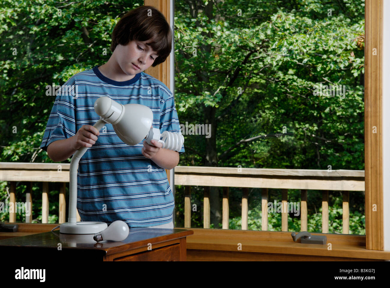 An eleven year old boy replaces a household incandescent lightbulb with an energy saving compact fluorescent bulb Stock Photo