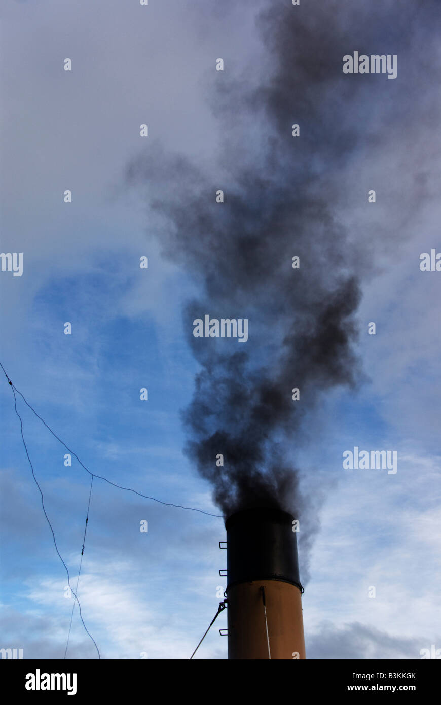 Dirty smoke rises from the funnel of a vintage coal burning tug. Stock Photo