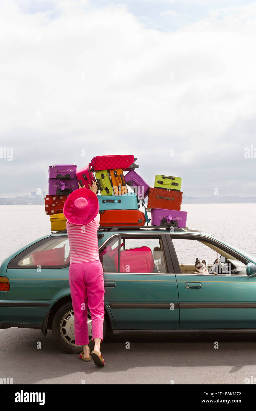 Woman adjusting stack of colorful suitcases on top of car Stock Photo