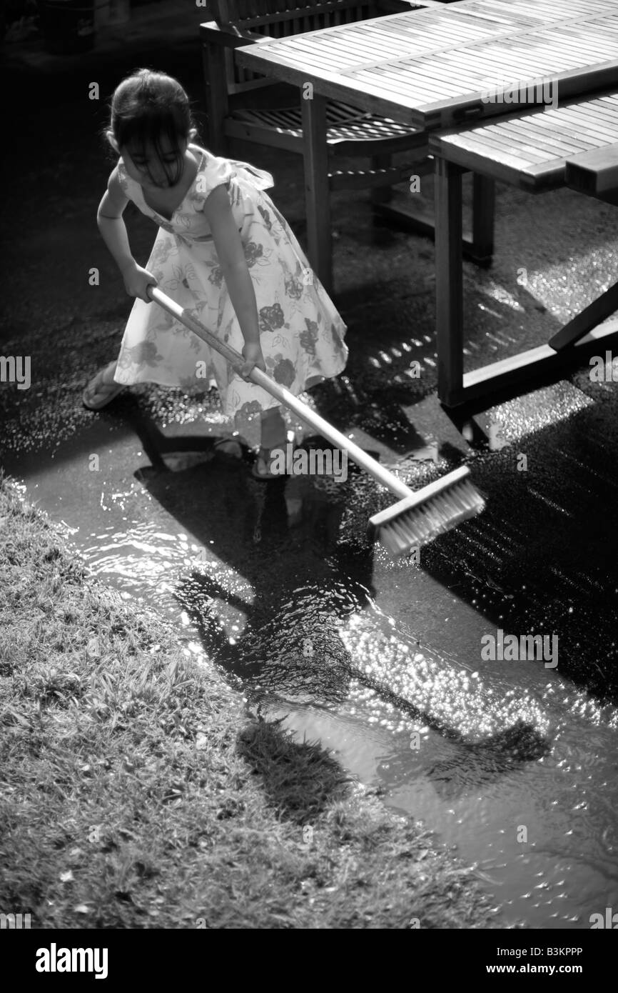 Sweeping away the water Girl aged five with broom Stock Photo
