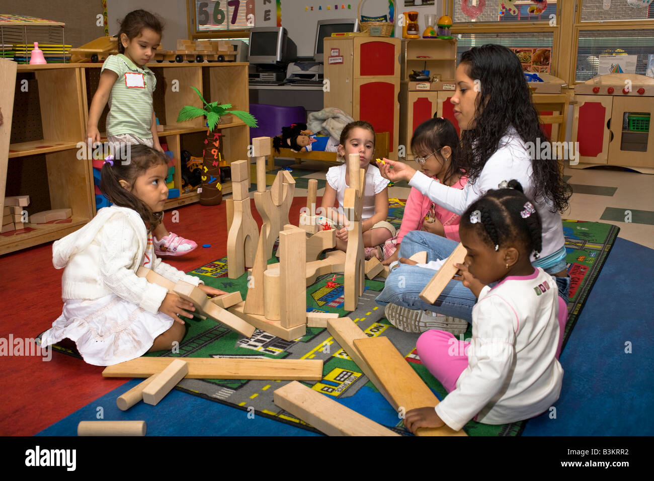 Female preschool teacher sitting on the floor playing with blocks with