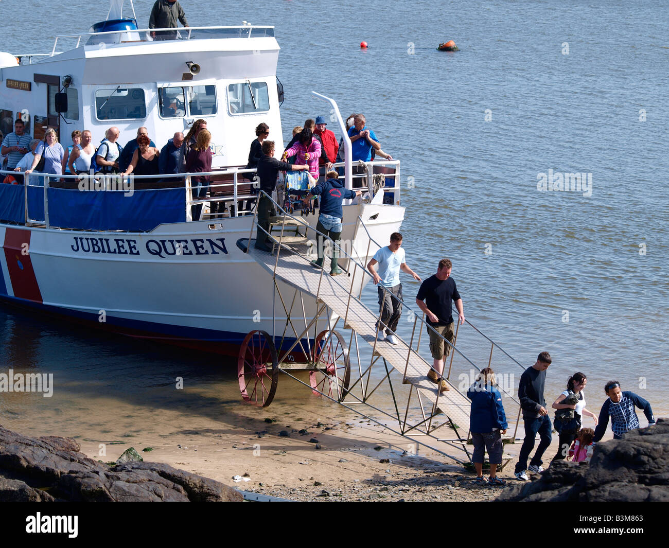 Passengers disembarking the Jubilee Queen tour ship, by way of a wheeled ramp which is pushed into the water to meet the ship. Stock Photo