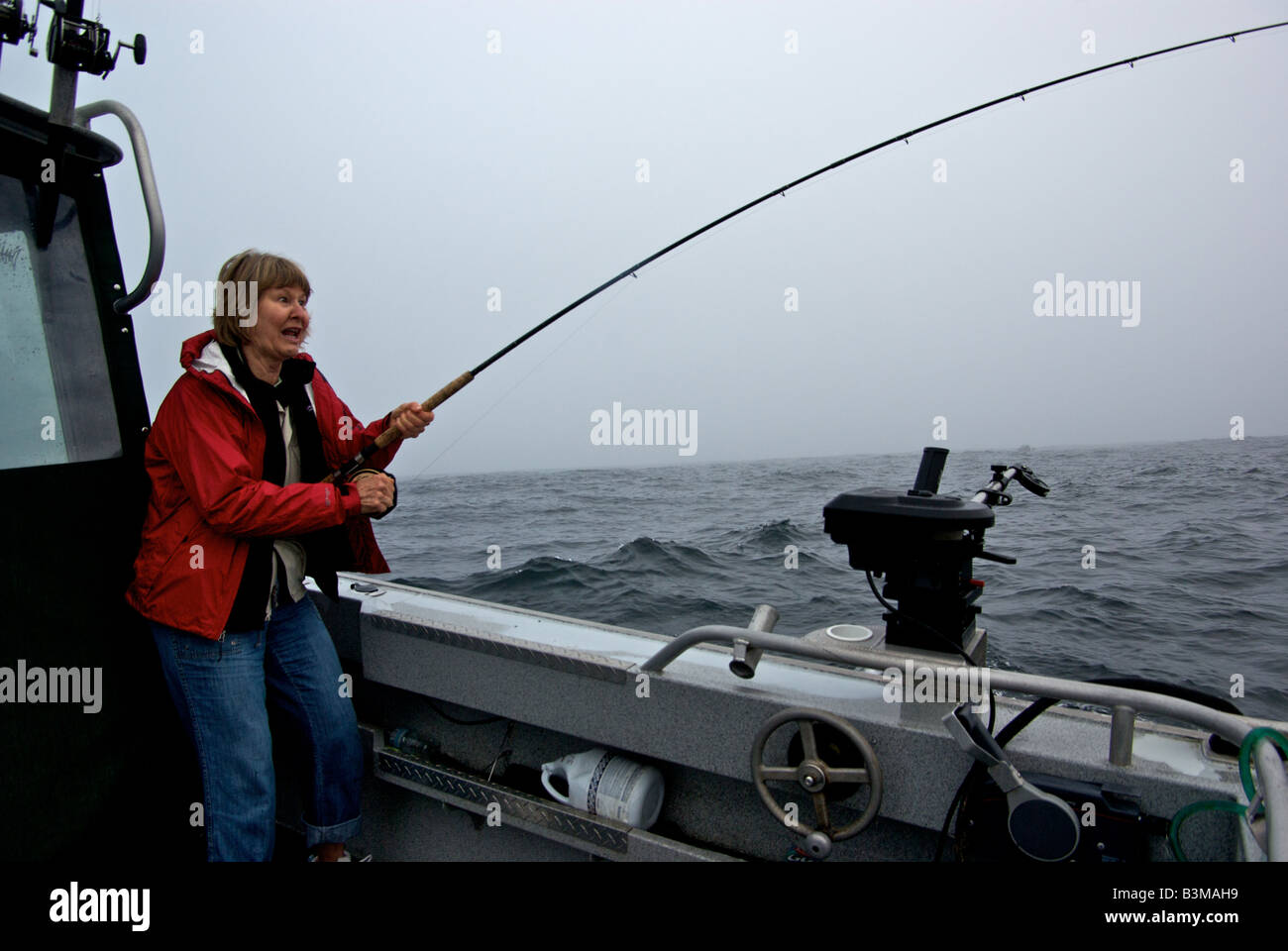 Woman angler with mixed emotions of terror and delight while playing her very first salmon in rough seas on a fishing charter Stock Photo