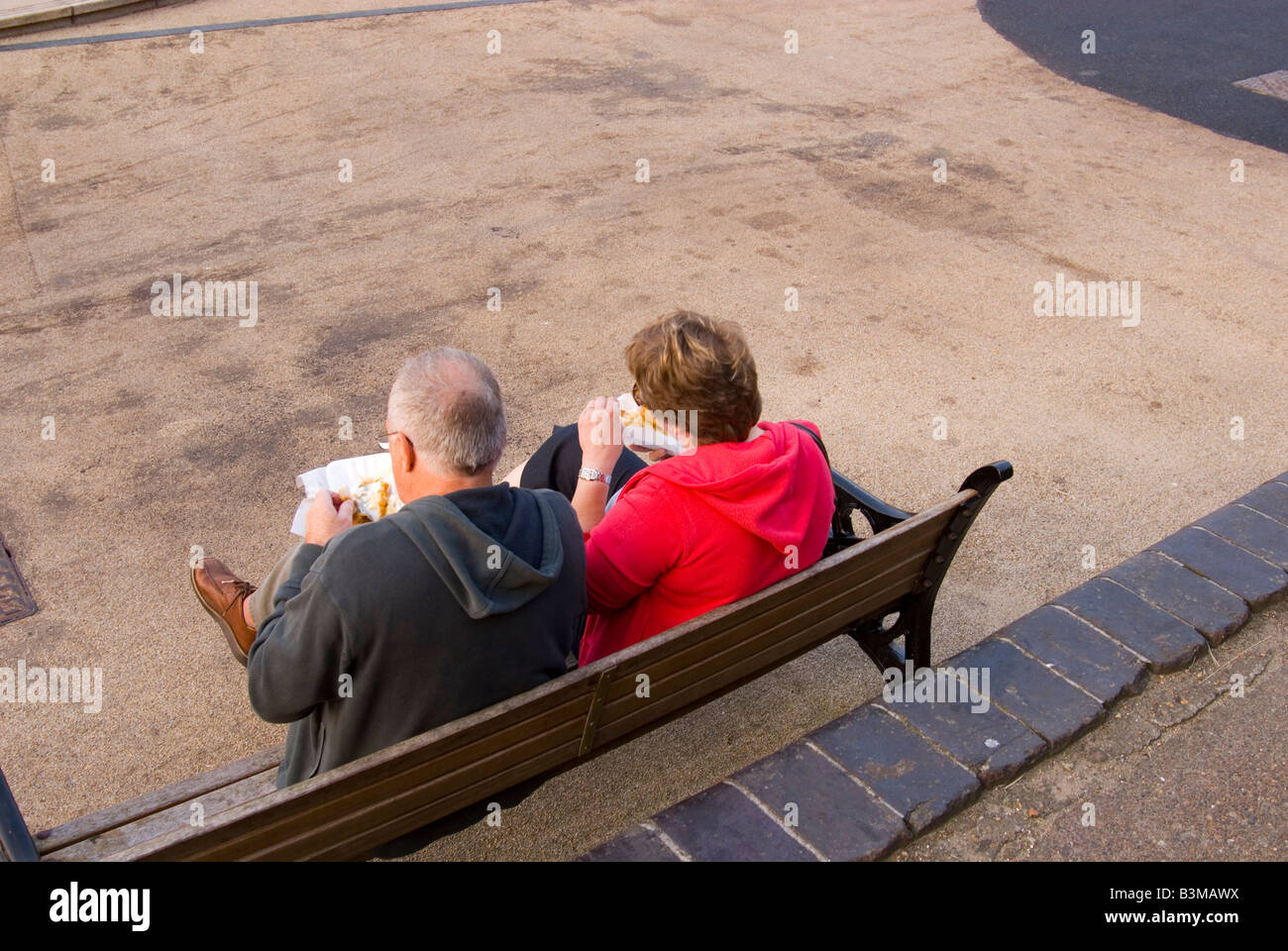 Middle aged couple eating fish and chips outside on a bench in the Uk Stock Photo