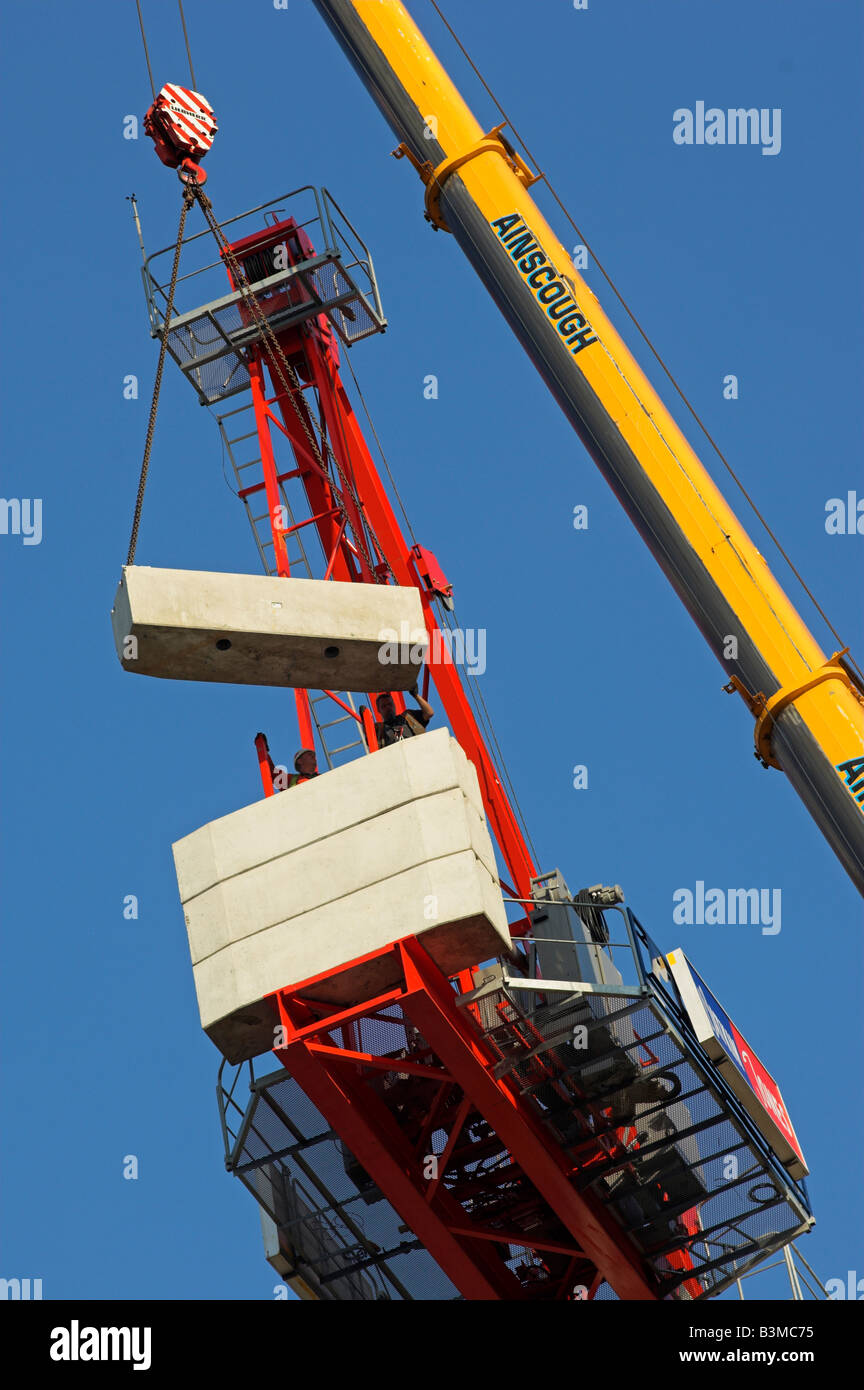 Hydraulic crane lifting concrete counterweight up to platform on tower