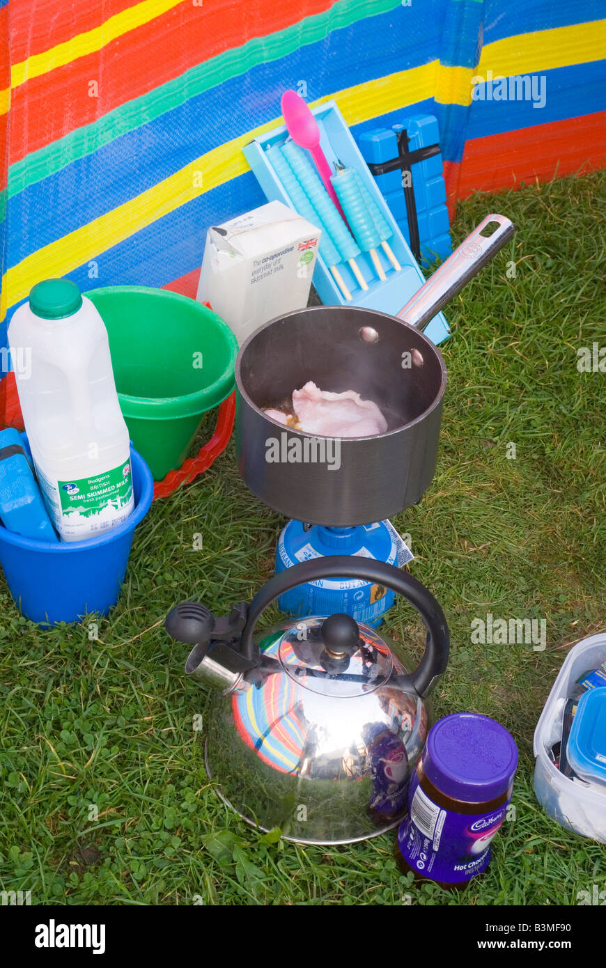 Camping stove cooking bacon in a saucepan outside,along with other camping bits and bobs Stock Photo