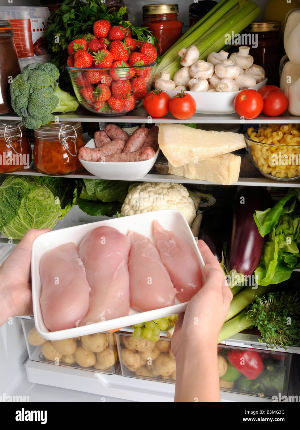 WOMAN TAKING CHICKEN MEAT FROM REFRIGERATOR Stock Photo