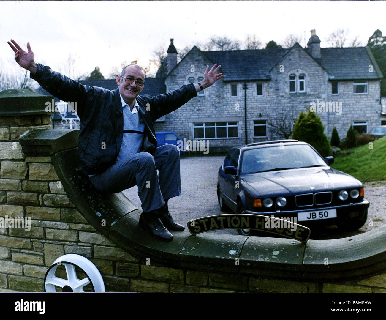 Jim Bowen comedian TV presenter sitting on his garden wall with arms outstretched Stock Photo
