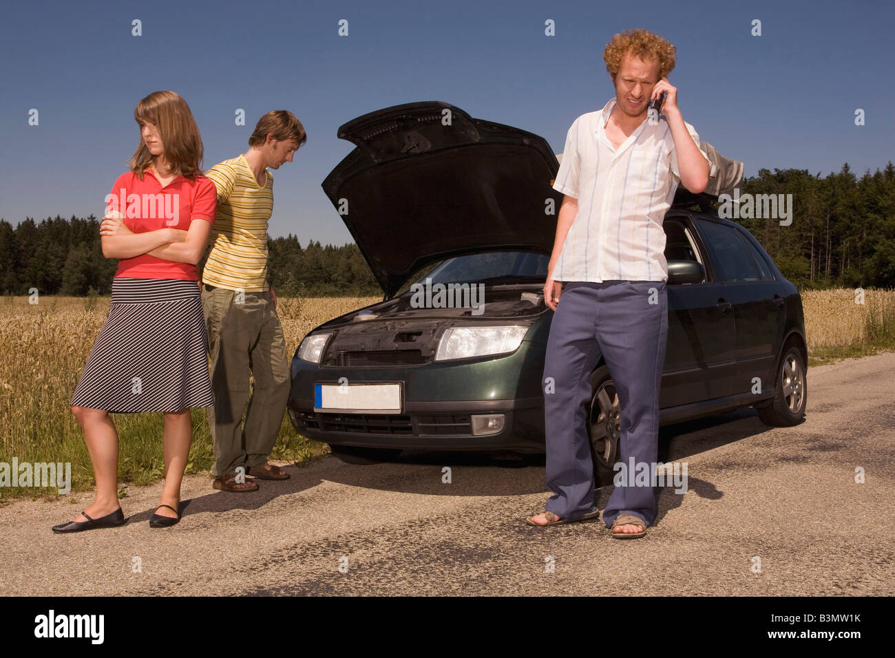 Germany, Bavaria, Three friends with broken down car Stock Photo