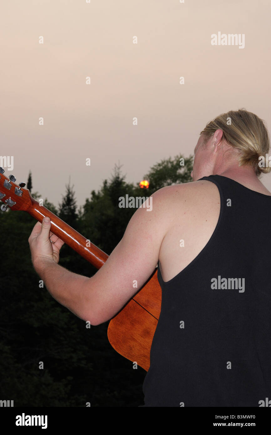 The Caucasian young man with blond long hair playing on acoustic guitar rear view Michigan MI pictures images photos vertical format in USA US hi-res Stock Photo