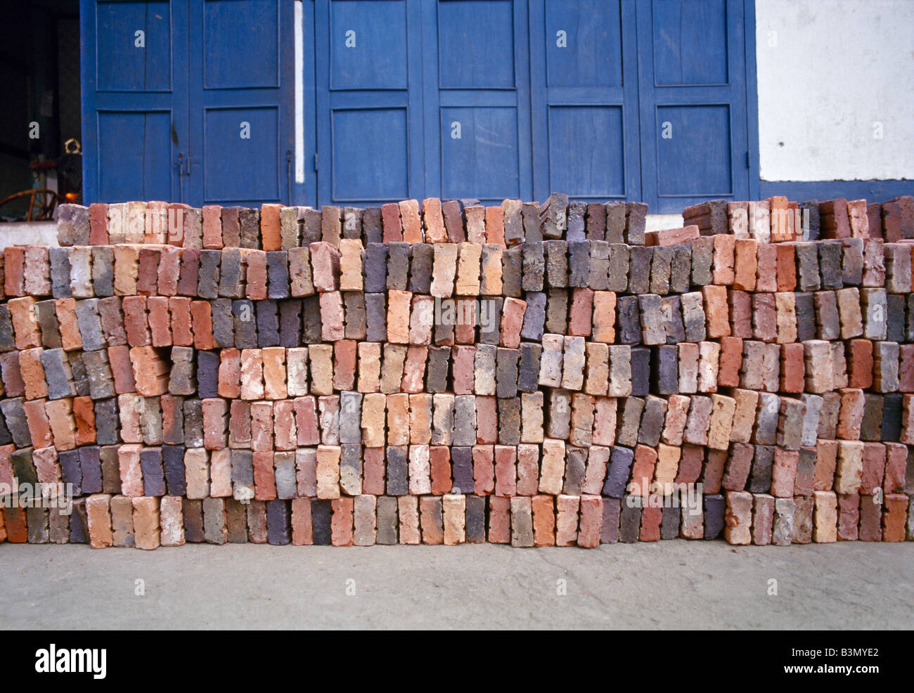 handmade multi coloured bricks in front of a blue wooden door in the former royal capital Luang Prabang in Laos Stock Photo