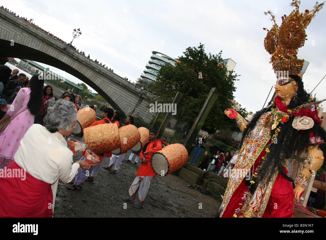 Musicians play drums and a woman dances in front of the deity Durga. Immersion ceremony, River Thames, Putney, London, England. Stock Photo