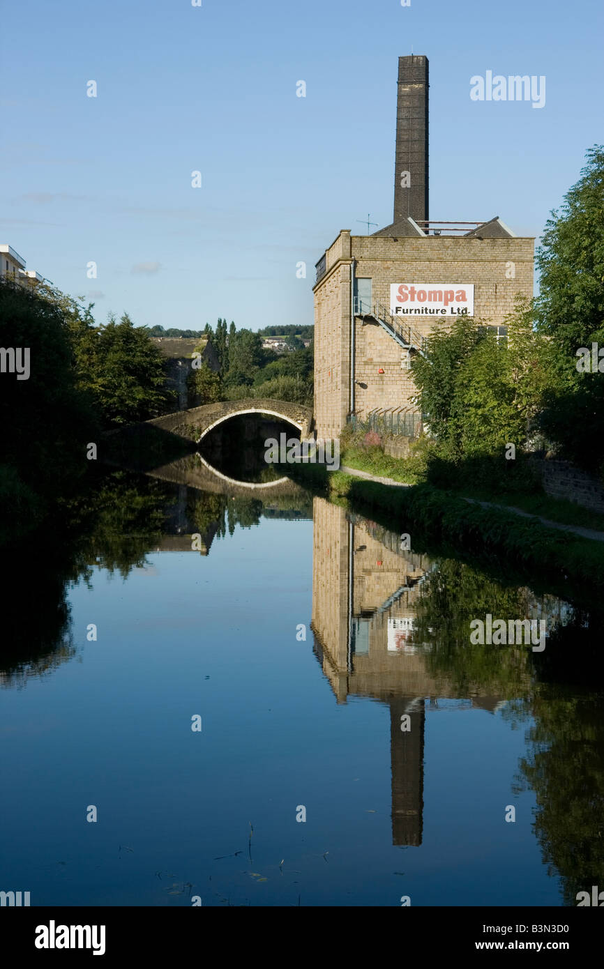 A factory chinmey and bridge are reflected in the Leeds-Liverpool Canal at Shipley, Bradford, West Yorkshire, UK Stock Photo