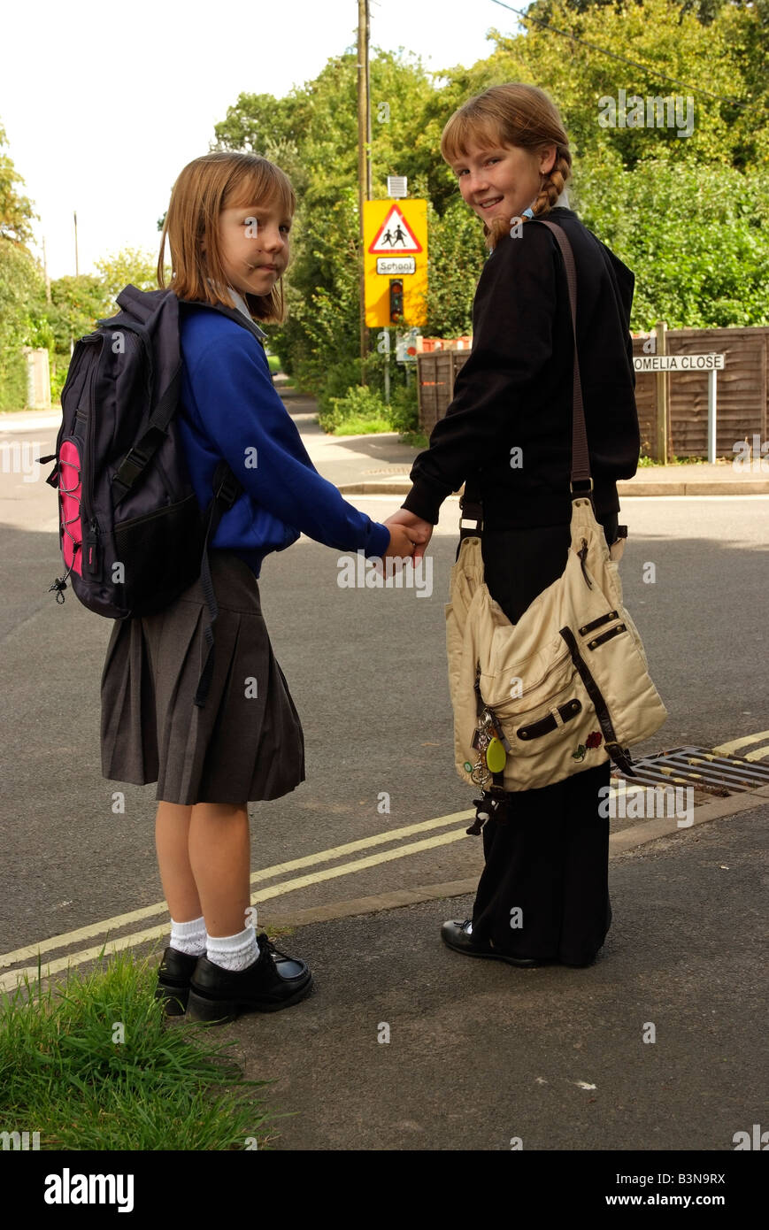Schoolgirls in uniform wait to cross a road on the school route England UK Road safety wait at the kerb before crossing a road Stock Photo
