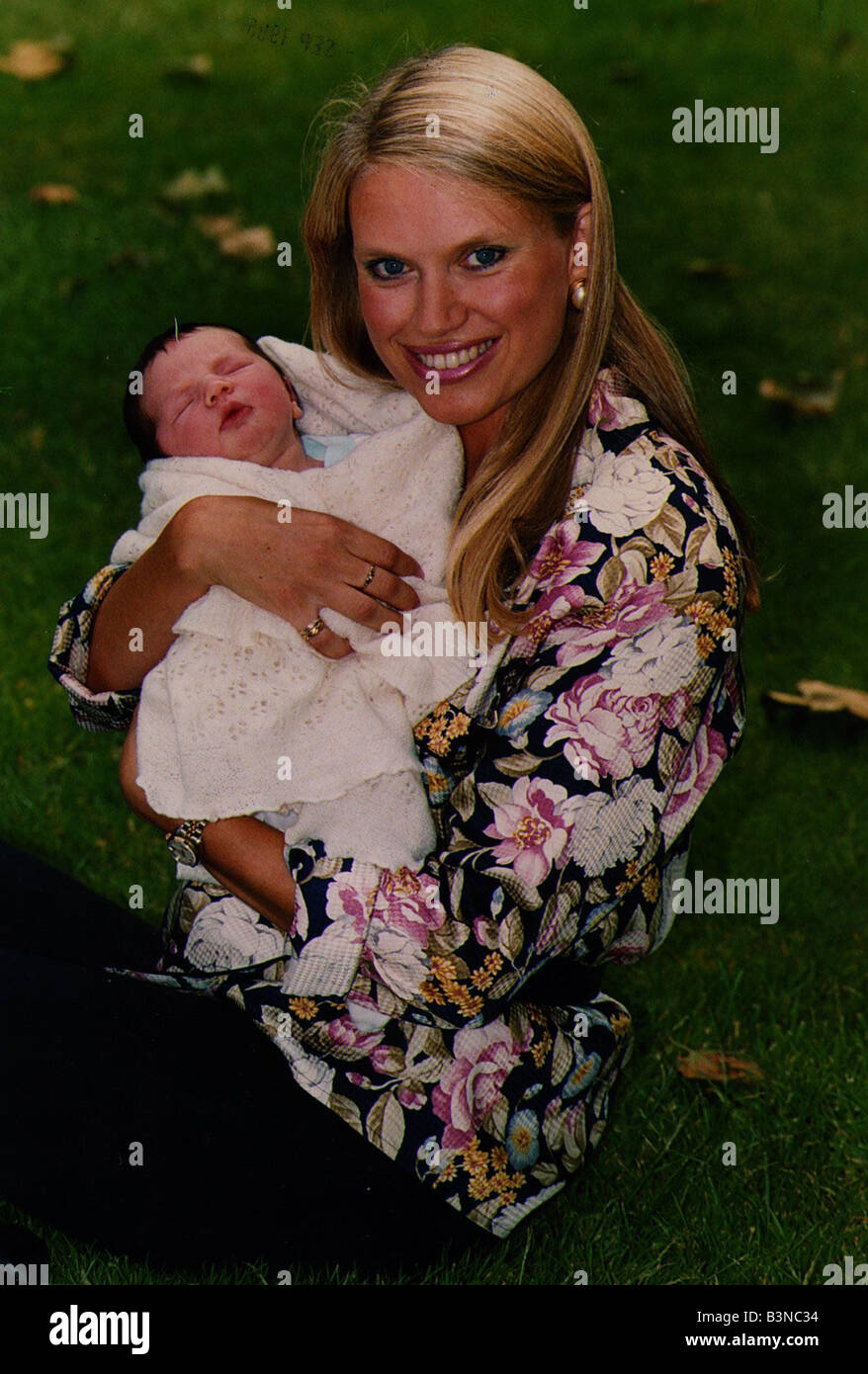 Anneka Rice holding baby smiling sitting on grass wearing flowery ...