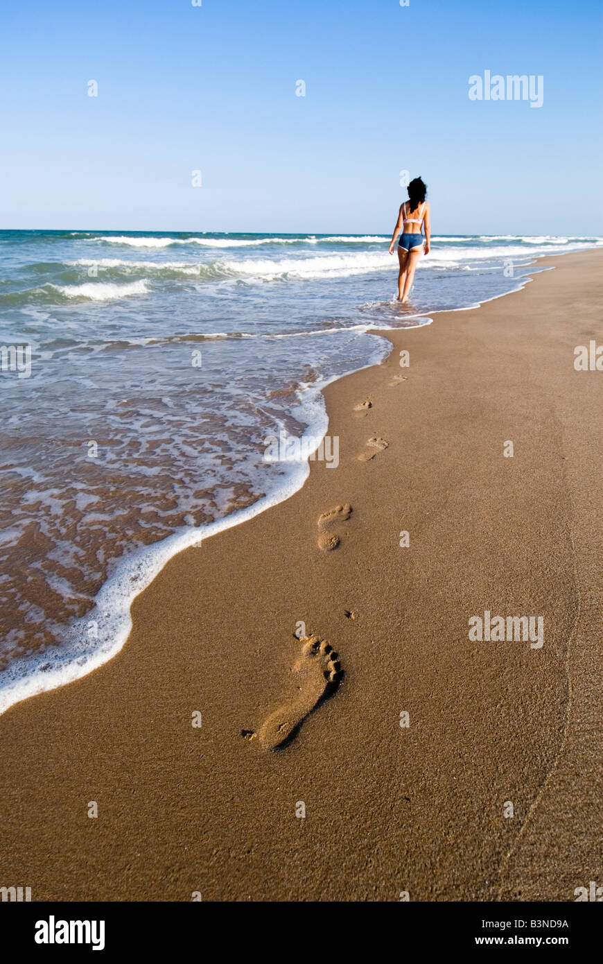Model Released Woman walking into the distance leaving footprints in the wet sand. El Saler. Valencia. Spain Stock Photo