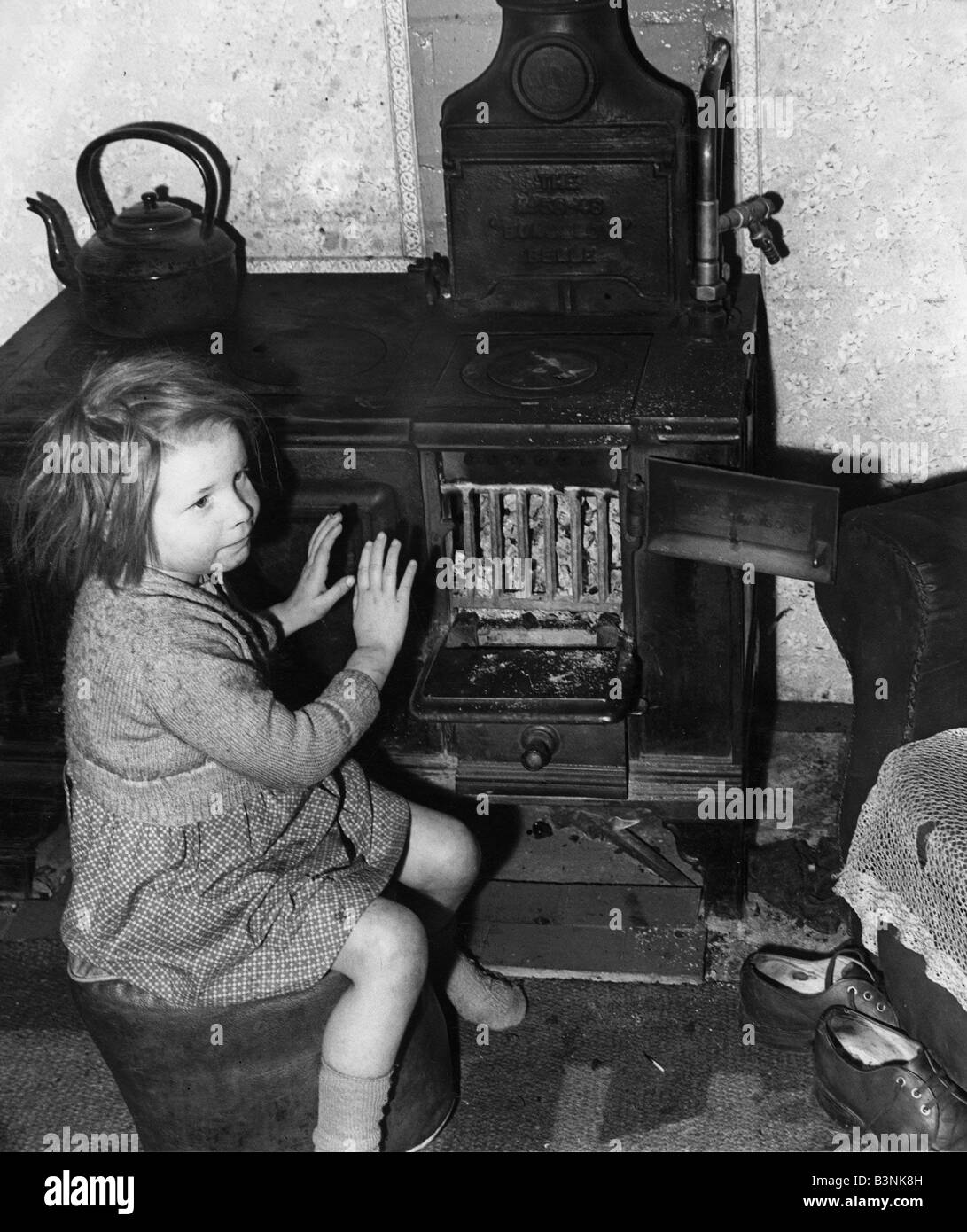 A young girl warms her hands by the oven February 1957 Stock Photo