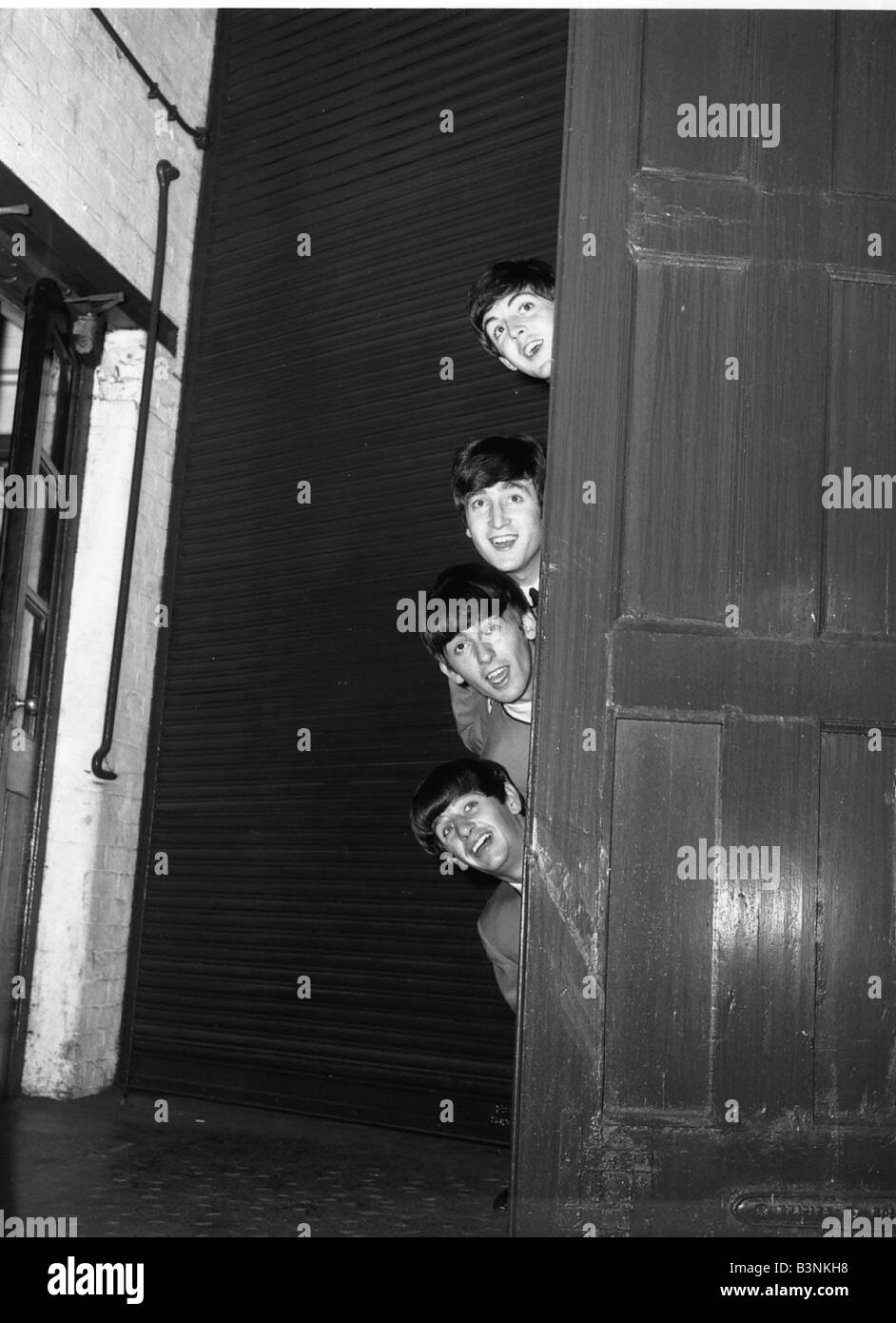Beatles peering out from behind a door in 1963 Stock Photo