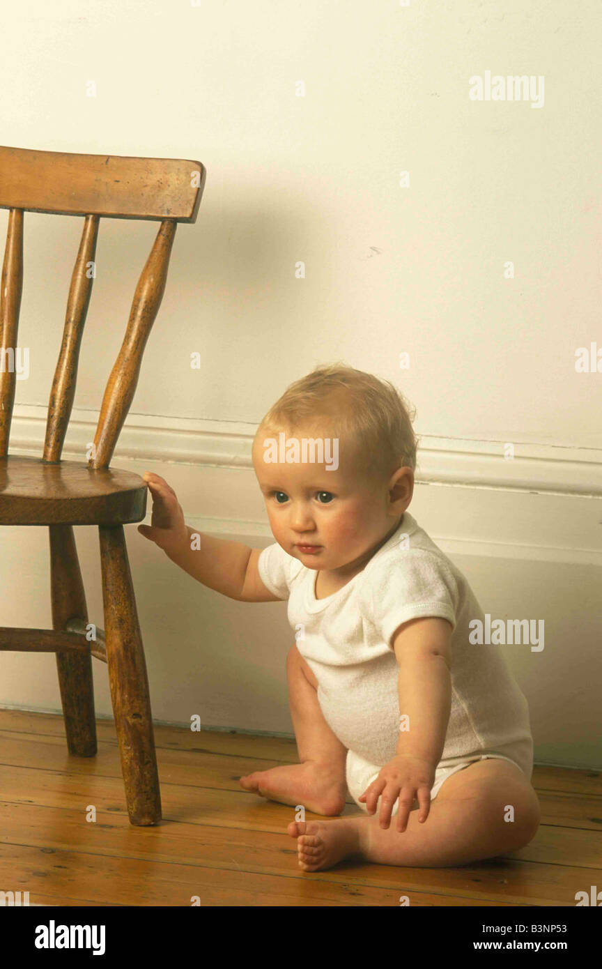 baby learning to stand pulling himself up with a small chair Stock