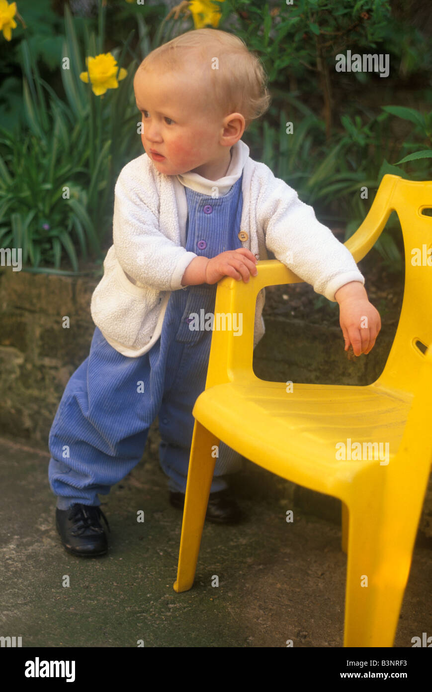 baby learning to stand pulling himself up with a small chair Stock