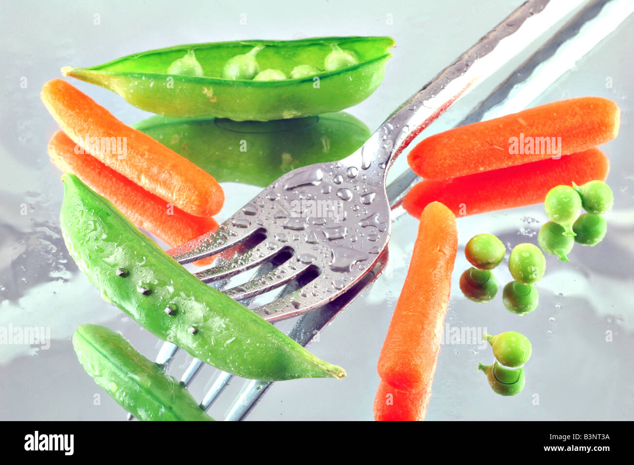 Fresh sugar peas and baby carrots on a mirrored background with a fork Stock Photo