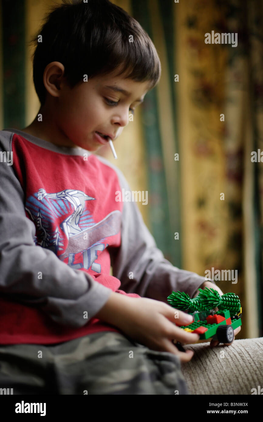 Boy aged six sucks lollipop while building toy with plastic bricks Stock Photo