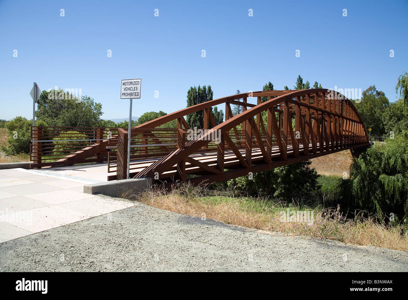 A steel foot bridge allows passage over a creek on a public walking path. Stock Photo