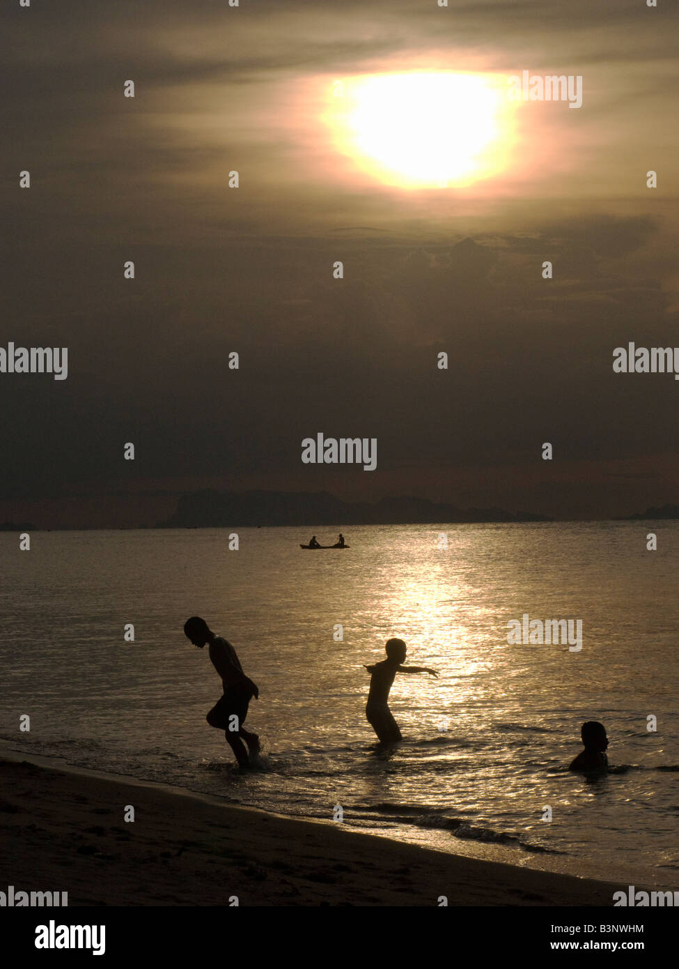 Three boys playing in the sea at sunset Stock Photo - Alamy