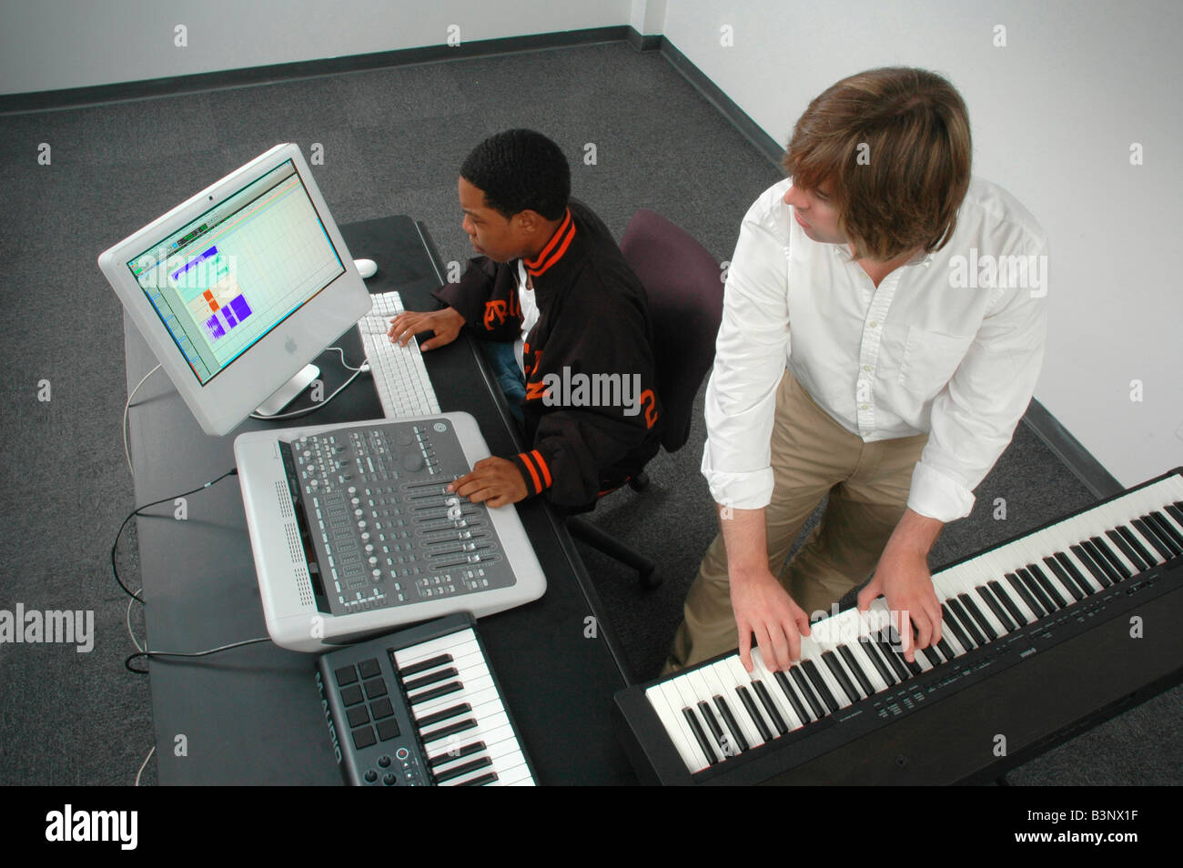 Two men in an audio production session one at keyboard the other at the mixing board Stock Photo
