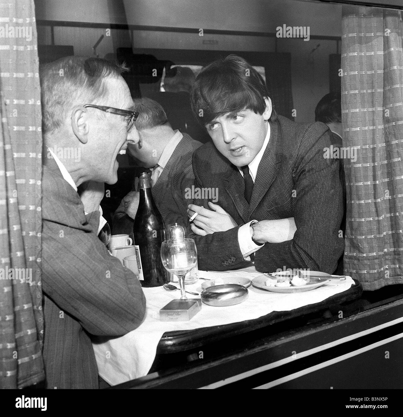 The Beatles March 1964 Paul McCartney and actor Wilfred Bramble chat at dining table on the train to South Molton Devon in the special train for the filming of A Hard Day s Night Stock Photo