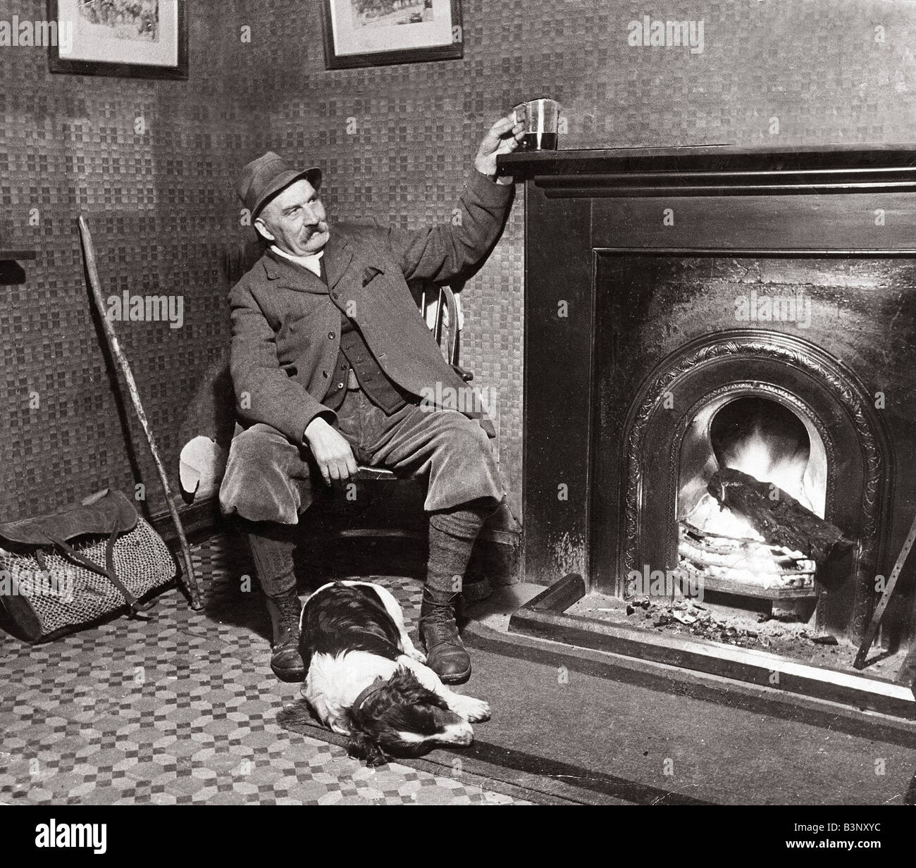 Man and his Dog March 1935 A game keeper relaxes with his drink by the fire at the Hampden Arms public house with his Dog Clothing Plus Fours Keep Bag Stock Photo
