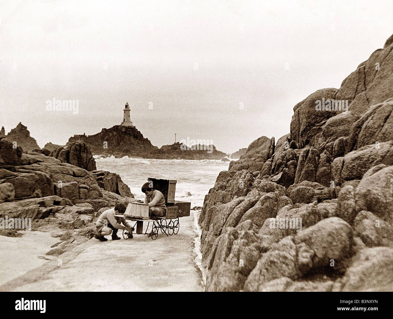 The two sons of the Corbiere Lighthouse keeper play on the causeway that leads to the light where their father spends most of his time Two boys playing with soapbox cart Toys Navigation Shipping English Channel Channel Islands Jersey February 1935 Stock Photo