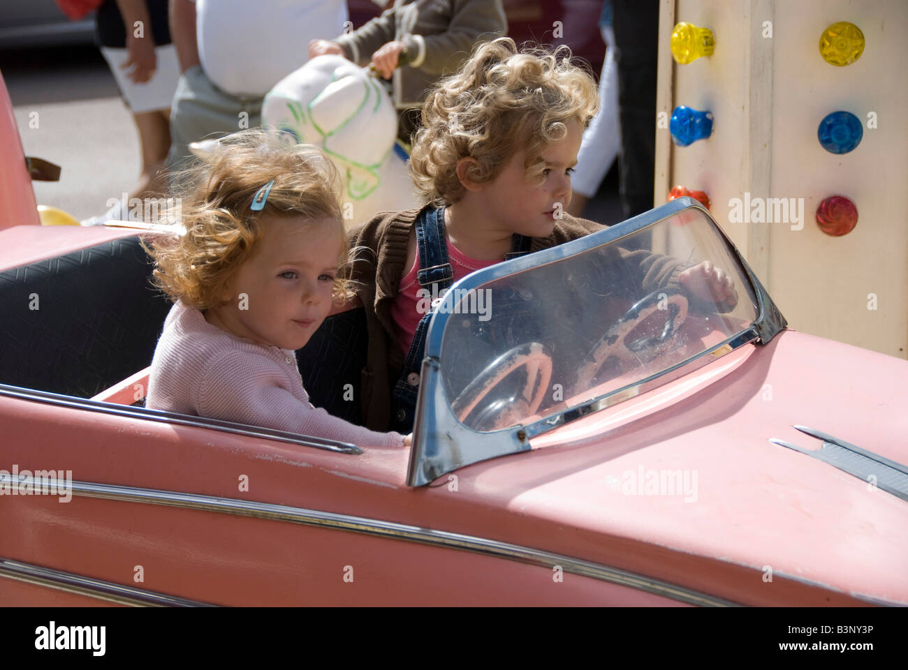 Barneville, Normandy, France. Two little girls in a pink model Cadillac on a merry go round (carousel) in the weekly market Stock Photo