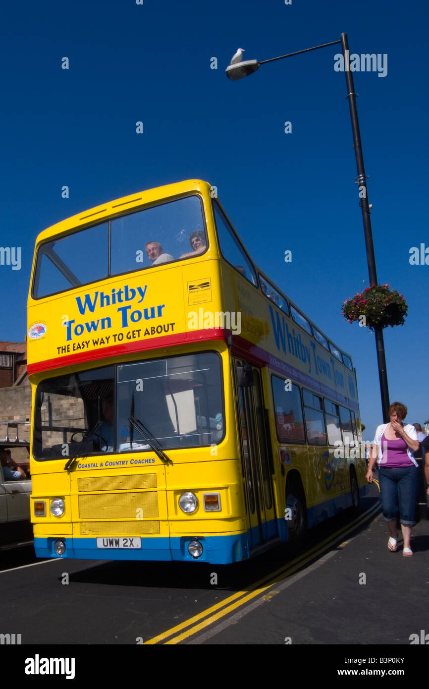 A bright yellow open topped double decker bus taking tourists on a tour around the seaside town of Whitby North Yorkshire UK Stock Photo