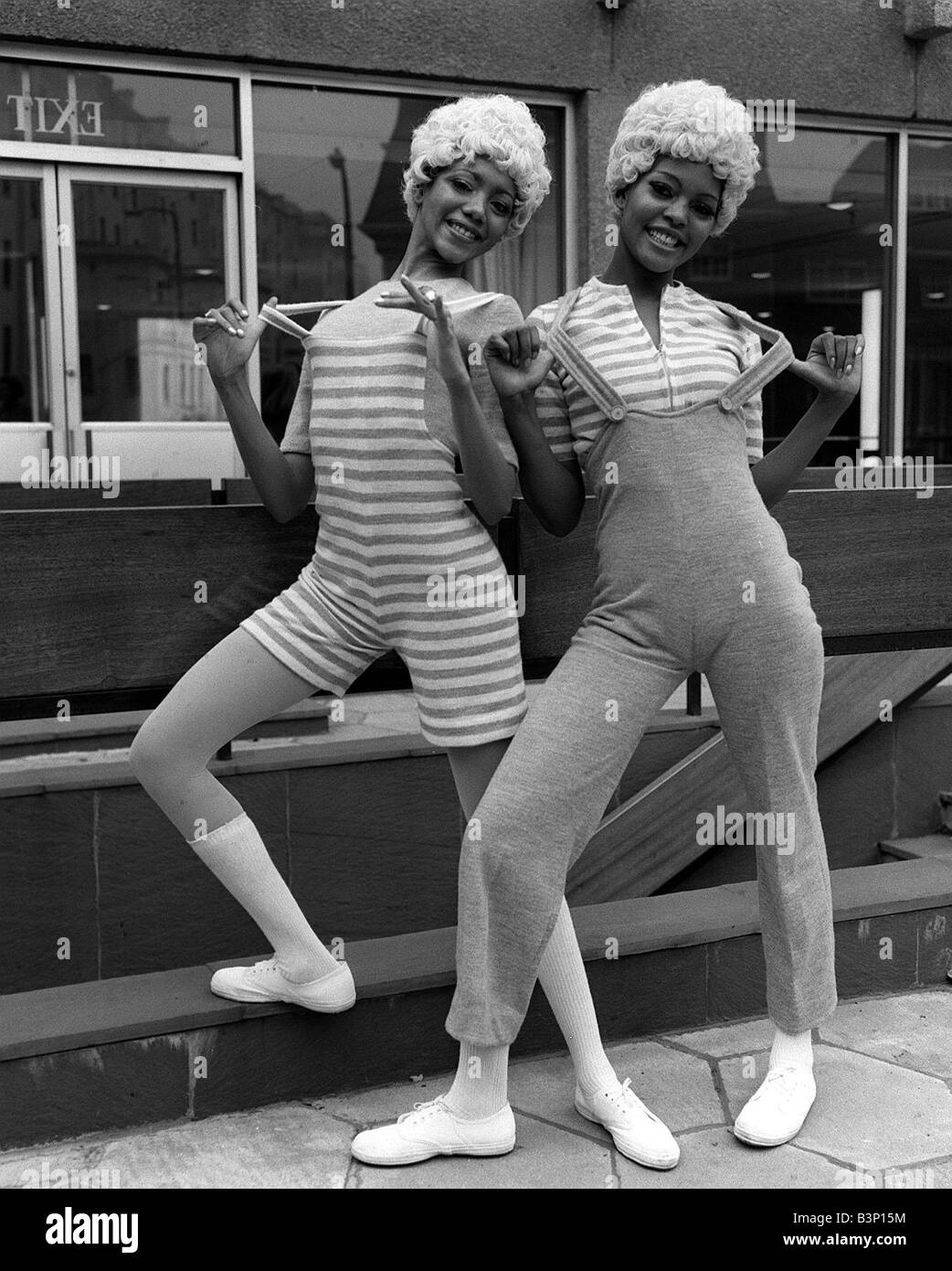 Two knitted outfits by Marlborough Hazel left in biband brace culotte outfit and Kubi in dungaree outfit African Caribbean models with blond hair posing together Stock Photo