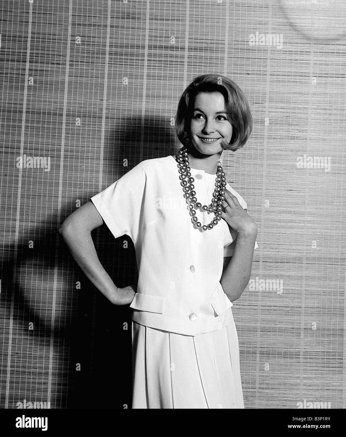 1960s Fashion Clothing April 1961 Sandra Paul Model Pictured wearing white suit and jumbo size gold beads Stock Photo