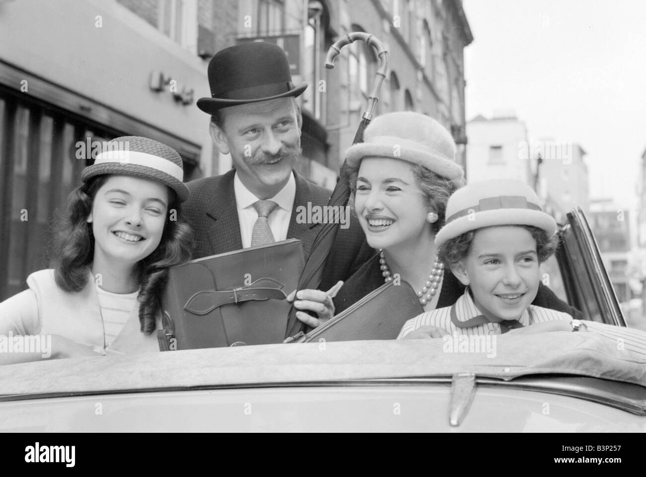 Hats by Milliner Victor Hyett seen here modelled in a London street prior to the 1959 Childrenswear Fair Models wearing straw hats Bowler hat sitting in car Clothing Fashion Hats Family Mother Father Daughters Businessman Umbrella Briefcase November 1959 1950s Mirrorpix Cyril Maitland 2 11 1959 L7984 Stock Photo