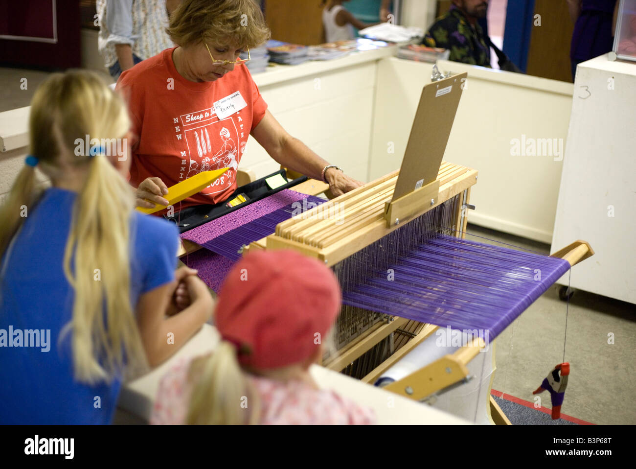 woman weaving on loom at New Mexico state fair as children observe Stock Photo