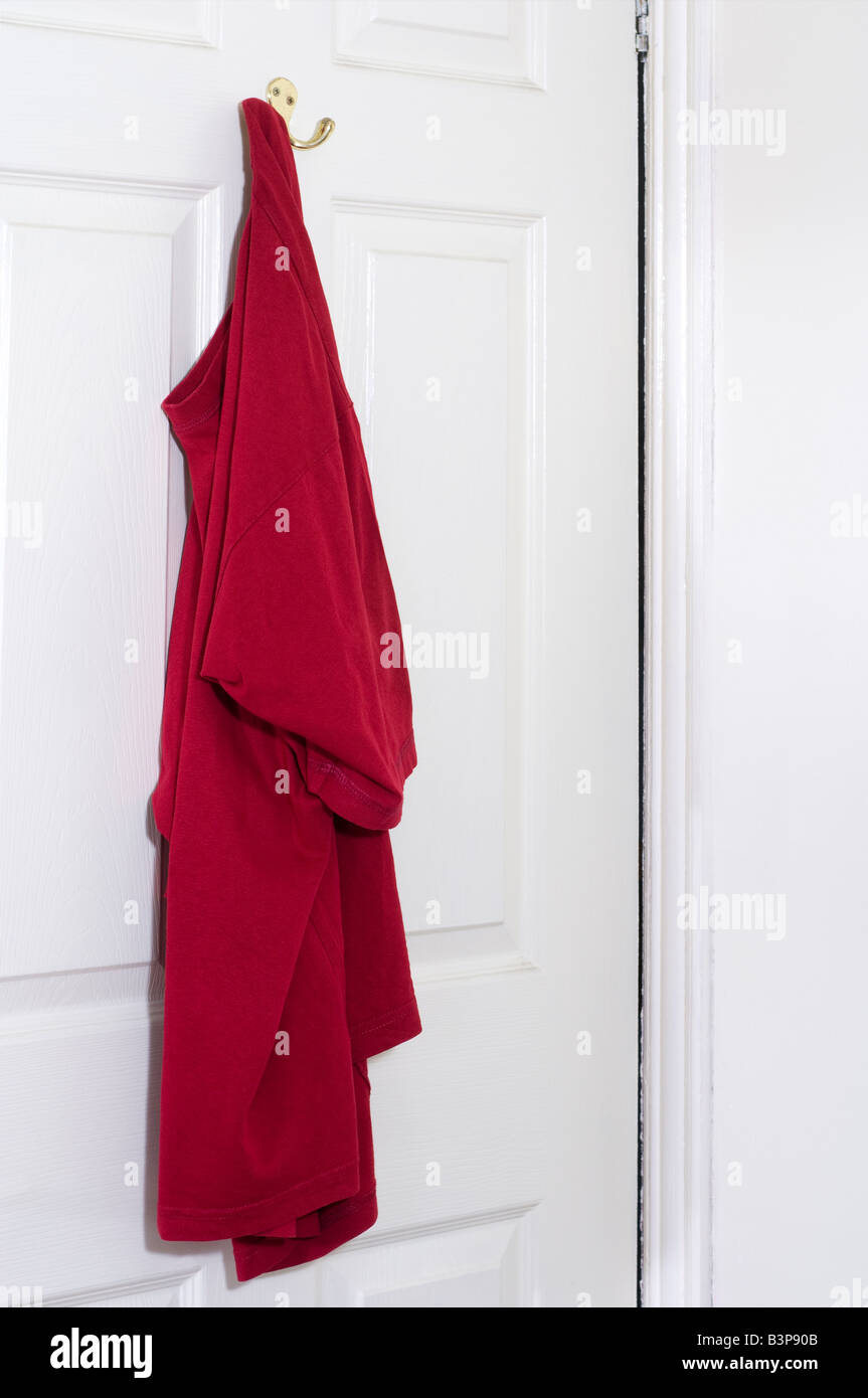 Mans red T shirt hanging on a hook on the back of a white door Stock