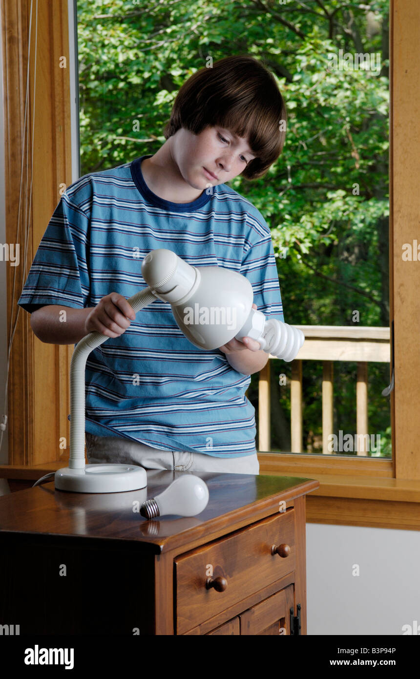 An eleven year old boy replaces a household incandescent lightbulb with an energy saving compact fluorescent bulb Stock Photo