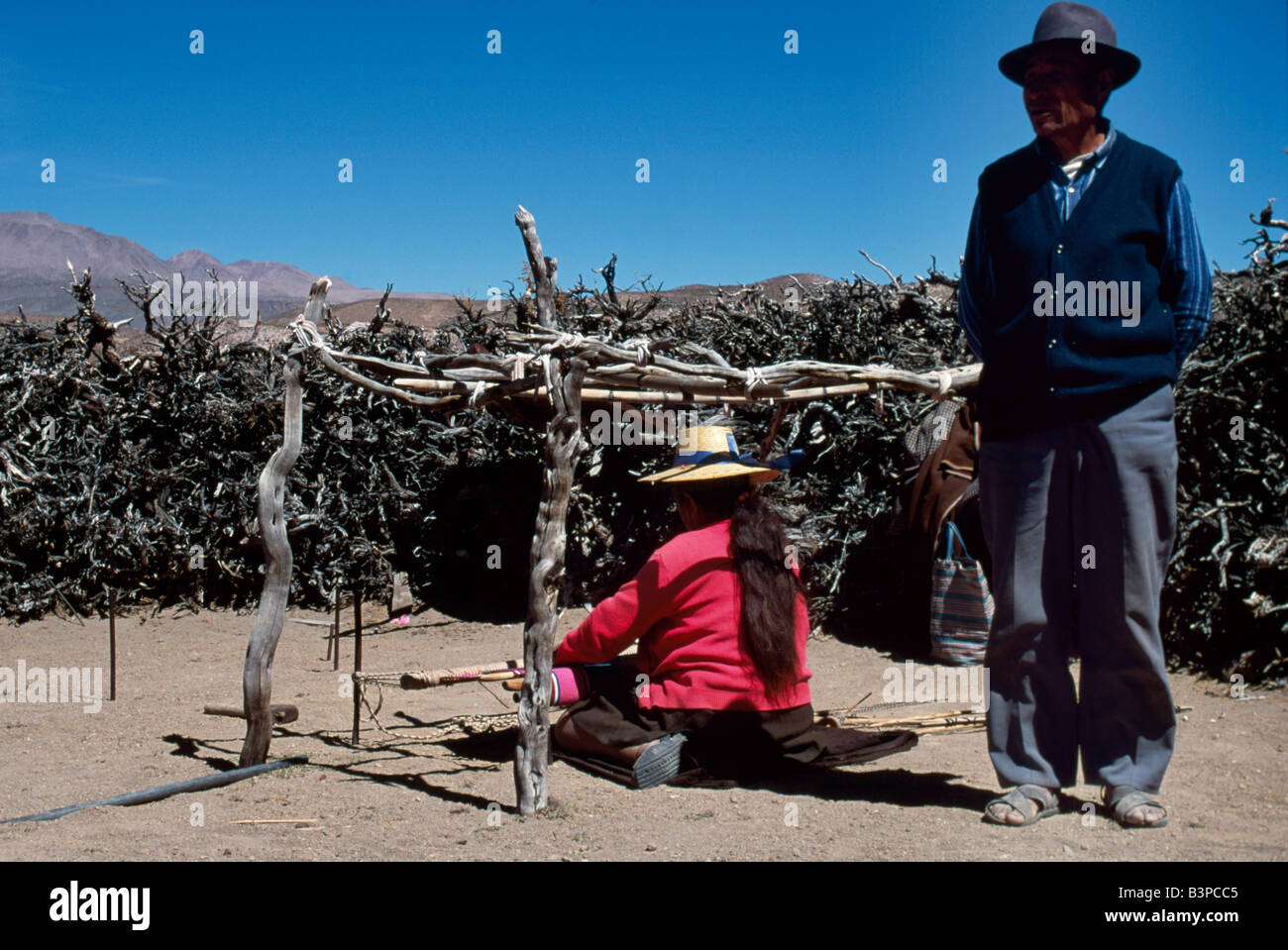 Chile, Region II, Parque Nacional Volcan Isluga. An Aymara man stands beside his wife who is weaving fabric Stock Photo
