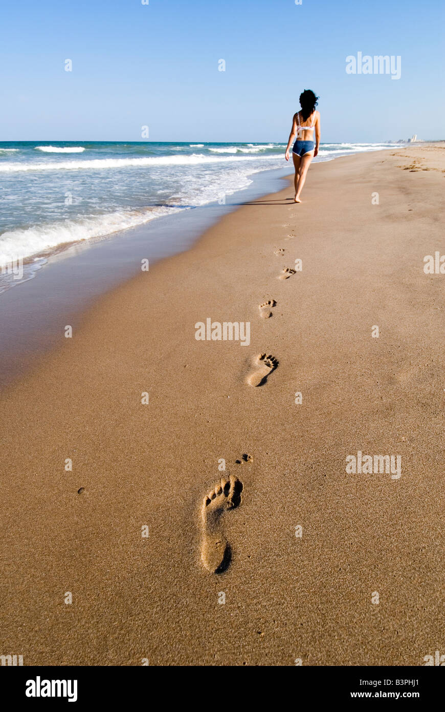 Model Released Woman walking into the distance leaving footprints in the wet sand. El Saler. Valencia. Spain Stock Photo