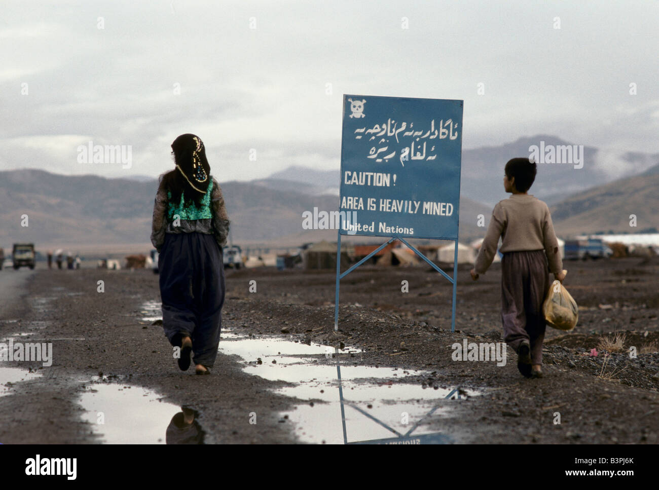 KURDISTAN', TWO PEOPLE WALKING PAST UNITED NATIONS SIGN WARNING OF THE DANGER OF UNEXPLODED MINES, PENJUIN, OCTOBER 1991 Stock Photo